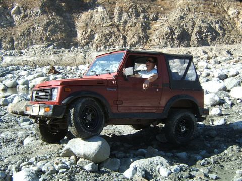 1988 Ford Bronco - Suzuki Samurai navigating rough terrain with a driver behind the wheel.