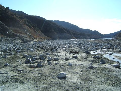 1988 Ford Bronco - Tire tracks mark the sandy and rocky terrain of a dry riverbed under a clear sky.
