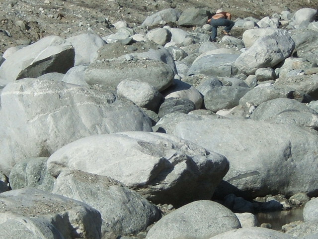 Person crouching on a rocky, dry riverbed with large boulders