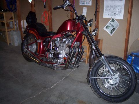 1973 Honda CB750K - A custom chopper motorcycle with a deep red metallic paint job and prominent chrome exhaust headers is parked indoors.