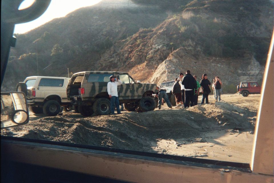group of people by a camo Bronco and a white SUV on a dirt hill