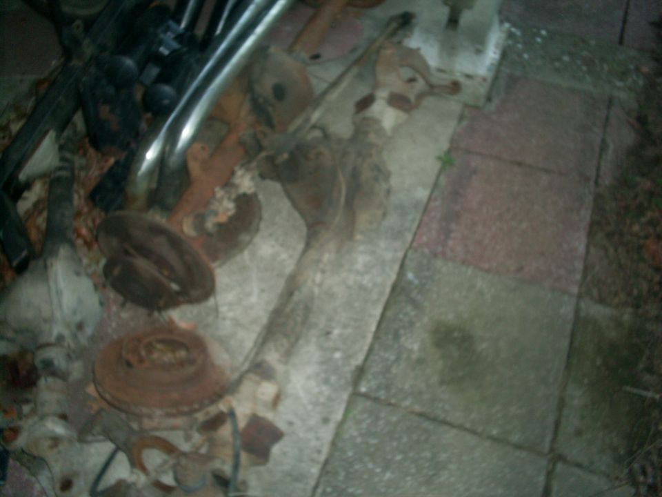 Rusty solid front axle with brake rotors and steering parts lying on concrete pavers