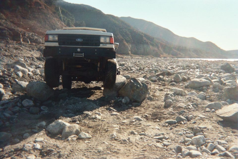 White 1987 Ford Bronco with a black bumper and winch, angled on a rocky, dry riverbed