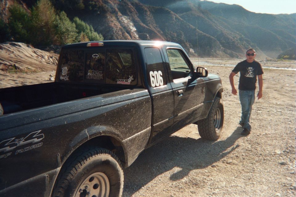 Black pickup truck with '4x4 Off Road' decal and '606' on the door, parked on a dirt road with mountains in the background