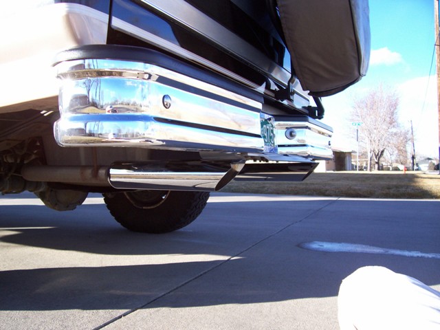 Low view of chrome rear step bumper, hitch receiver and exhaust tip on a dark SUV