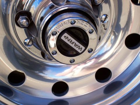 1996 Ford Bronco - A close-up view of a chrome wheel a Warn locking hub, indicating it is part of a vehicle's drivetrain.