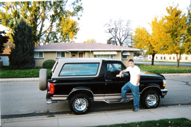Black Ford Bronco with tan top and rear spare tire parked at a suburban curb
