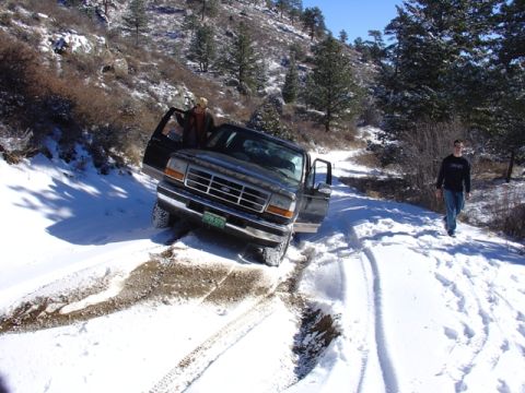 1996 Ford Bronco - A dark Ford truck is stuck in the snow on a mountain road with two people nearby.