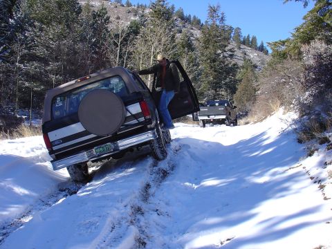 1996 Ford Bronco - A man enters a Ford Bronco that is stuck in the snow on a wooded road, with another vehicle following behind.