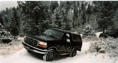 1996 Ford Bronco - Black 1996 Ford Bronco navigates a snow-covered forest road with a second vehicle behind it.