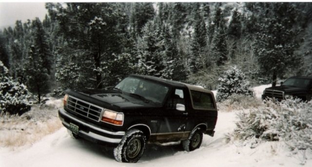 1996 Ford Bronco driving on a snowy trail with another SUV visible in the background