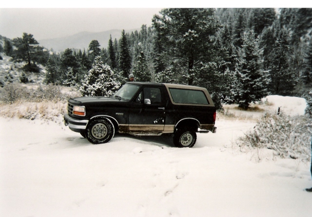 Black Ford Bronco parked in snow with trees in background
