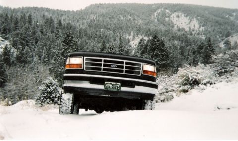 1996 Ford Bronco - A black 1992 Ford Bronco navigates a snow-covered mountain road, its tires kicking up snow.