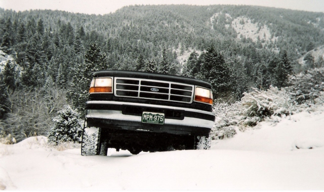 Front view of a black 1992 Ford Bronco driving on a snowy road