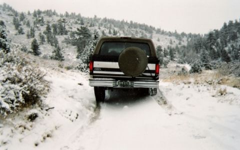 1996 Ford Bronco - Ford Bronco driving on a snowy mountain road with trees in the background.