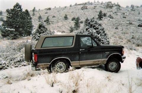 1996 Ford Bronco - A 1996 Ford Bronco navigates a snowy, hilly terrain with sparse trees.
