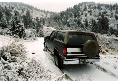 1996 Ford Bronco - A Ford Bronco navigates a snow-covered trail through a wooded hillside.