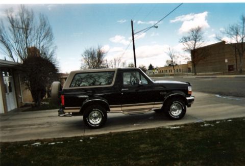 1996 Ford Bronco - A black Ford Bronco with tan accents is parked on a driveway under a cloudy sky.
