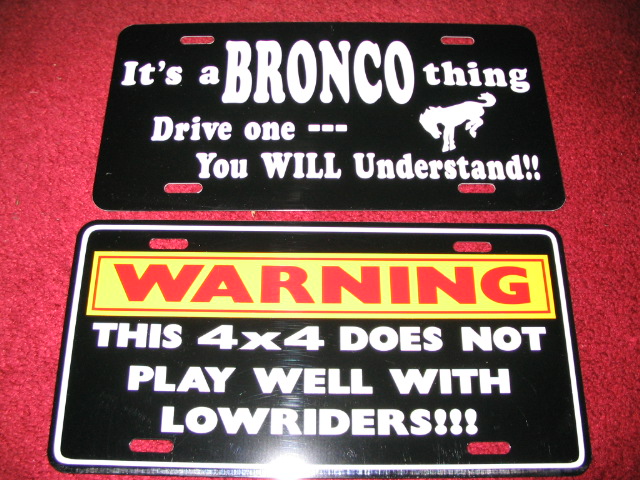 Two novelty license plates: "It's a Bronco thing" and a 4x4 vs lowriders warning