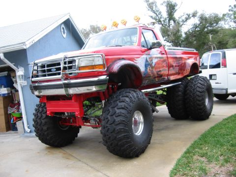 1974 Ford F-100 - Monster truck with custom paint and lifted suspension sits in a driveway next to a house.