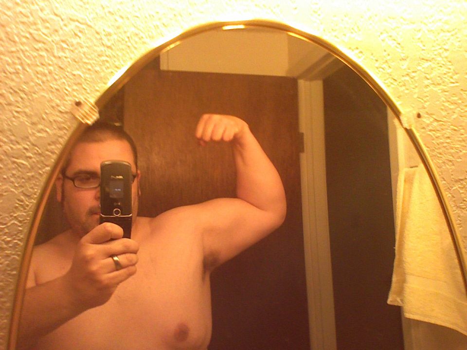 Man taking a flexing mirror selfie with a flip phone