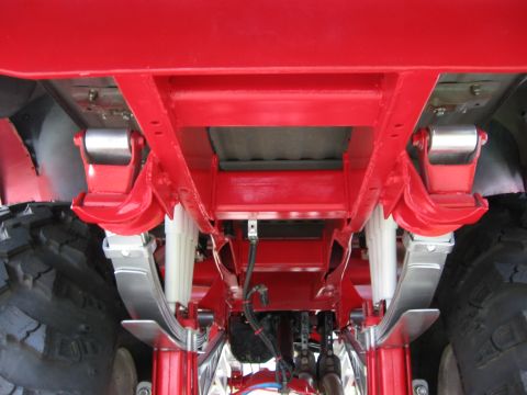 1974 Ford F-100 - The undercarriage of a red truck shows its suspension system with large tires on the sides.