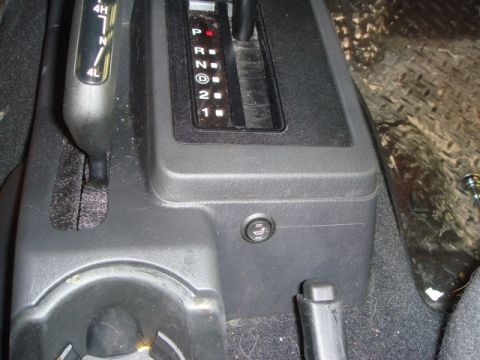 1996 Ford Bronco - Close-up of a vehicle's interior showing the gear shifter and a seat adjustment button on the center console.