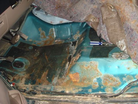 1996 Ford Bronco - The interior floor of a vehicle shows significant rust and corrosion, with insulation exposed.