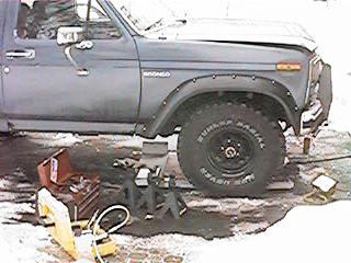 1986 Ford Bronco - A Ford Bronco is raised on jack stands with tools nearby, suggesting maintenance or modification work is underway.