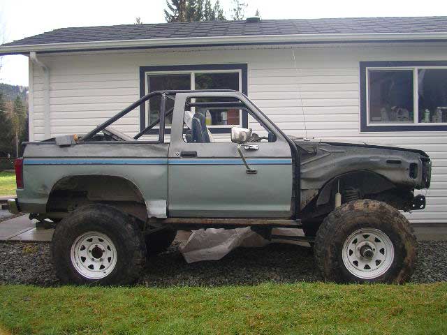 Side view of a light blue 1984 Ford Bronco II with a roll cage and missing front fender