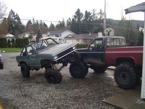1984 Ford Bronco II - Two heavily modified trucks are parked side-by-side on a gravel lot.