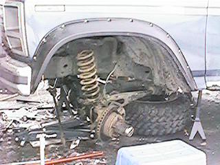 1986 Ford Bronco - Close-up of the front suspension and wheel well area of a vehicle, showing suspension components and fender flares.