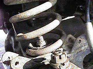 1986 Ford Bronco - This image shows a close-up view of a vehicle's suspension system, focusing on the coil spring and its attachment points.