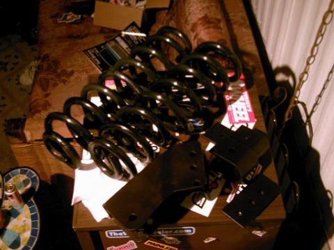 1986 Ford Bronco - A collection of suspension lift springs and mounting brackets are displayed on a table, some with various stickers.