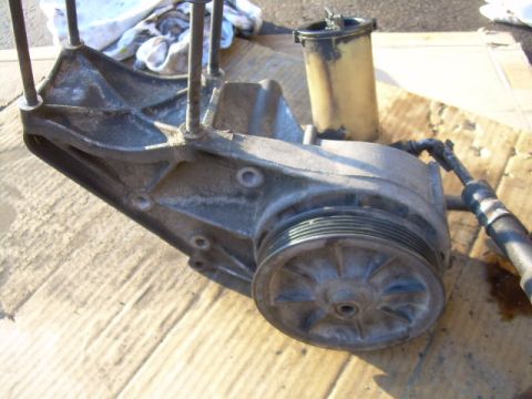 1992 Ford Bronco - A disassembled power steering pump assembly sits on a piece of cardboard, showing the pump, pulley, and reservoir.