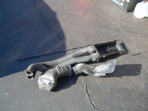 1992 Ford Bronco - Several disconnected air intake system components are laid out on a cracked asphalt surface.