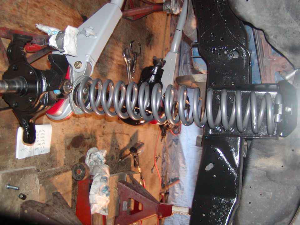 close-up of vehicle suspension parts, including springs and steering knuckle, in a workshop