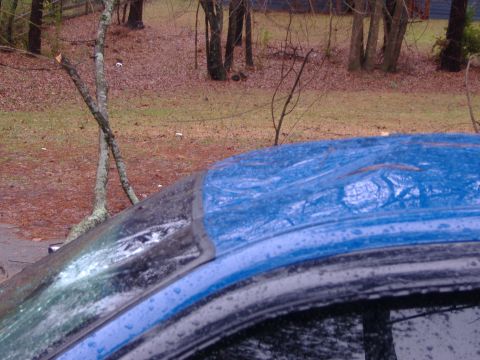 1998 Ford Crown Victoria - Close-up of a damaged blue car roof with water on its surface.