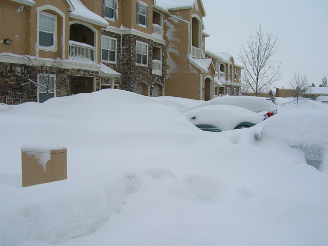 Cars buried in deep snowdrifts in front of apartment buildings