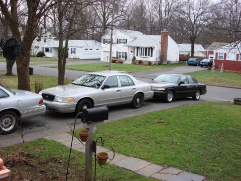 2003 Ford Crown Victoria - A silver 2003 Ford Crown Victoria is parked in a suburban driveway next to another car.