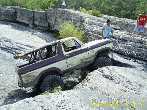 1979 Ford Bronco - A two-tone Ford Bronco navigates a rocky terrain, its tires covered in mud.