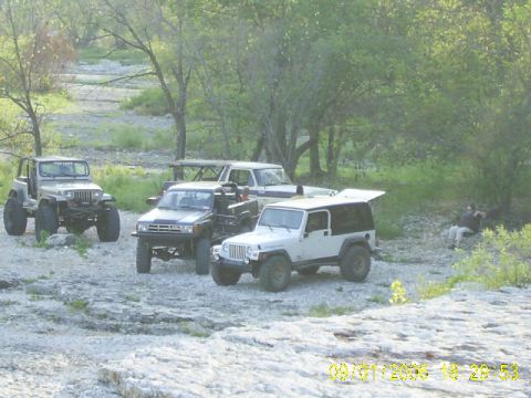 1979 Ford Bronco - A group of off-road vehicles are parked in a natural setting with trees and rocks.