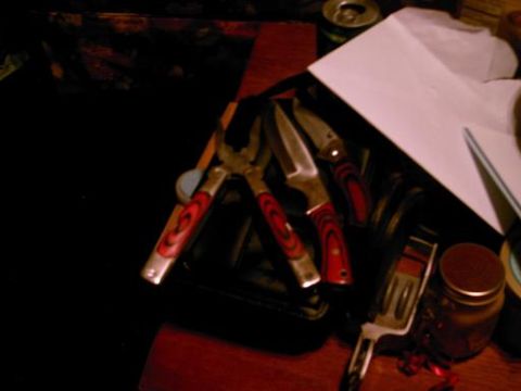 1986 Ford Bronco - A collection of knives and pliers with red and black handles are laid out on a surface.