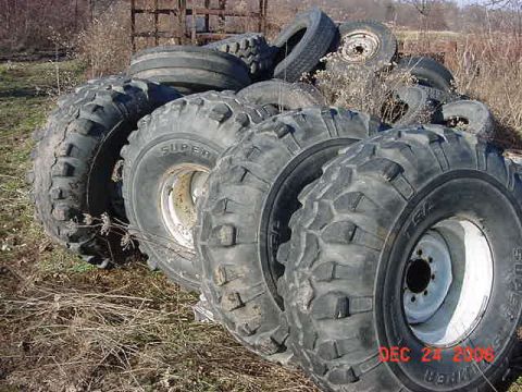 1977 Ford F-250 - A collection of various off-road tires are piled up outdoors, with a watermark indicating 'SUPERMOTORS'.
