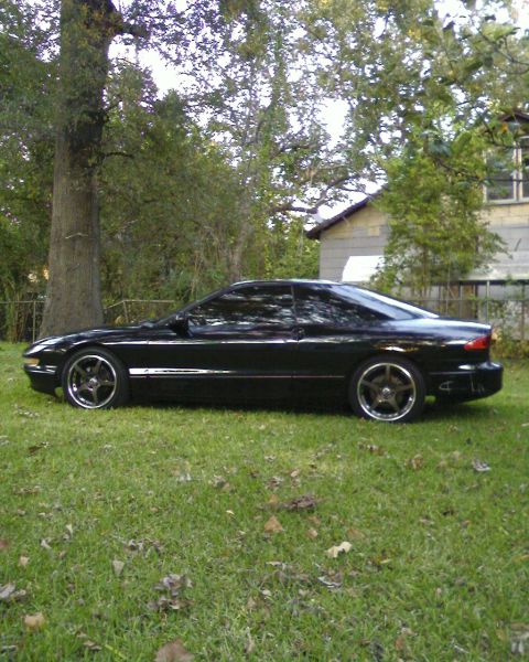 1996 Ford Probe - A black coupe is parked on a grassy lawn with trees and a house in the background.