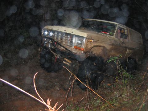 1992 Ford Mustang - A tan Ford Bronco with oversized tires is stuck in the mud off-road.
