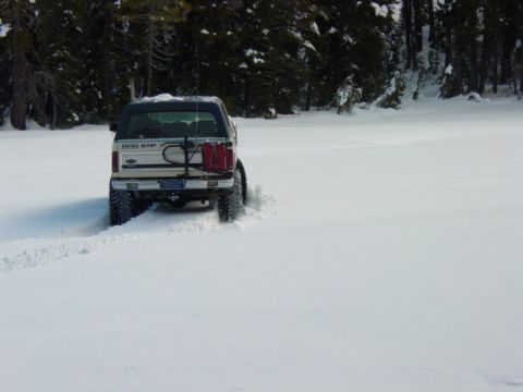 1986 Ford Bronco - 1986 Ford Bronco navigates a snowy landscape, kicking up snow as it drives.