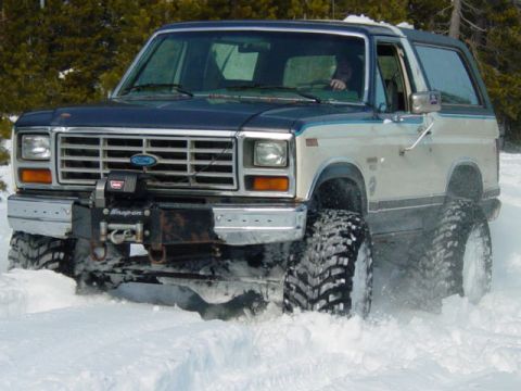1986 Ford Bronco - Ford Bronco with large tires driving through snow, front view. Winch mounted on bumper.