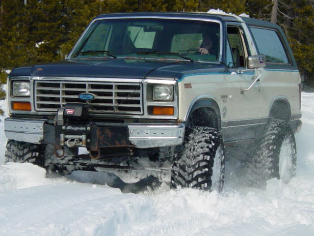 Ford Bronco with large tires driving through snow, front view. Winch mounted on bumper