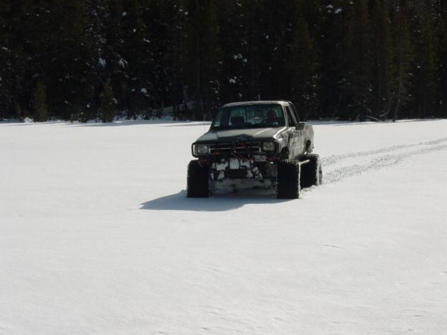 Gray pickup truck with oversized tires driving in snow